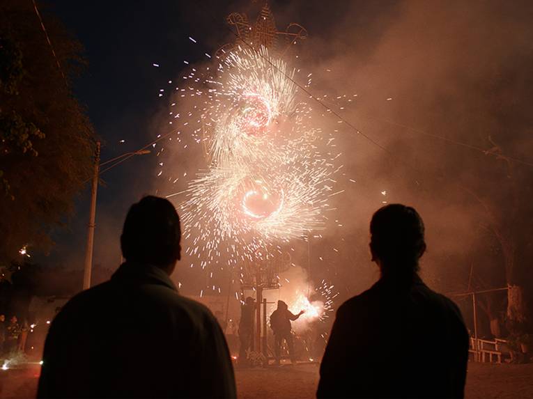 Zwei Personen schauen sich eine Art Feuerwerk an. Man sieht sie schattenhaft von hinten.